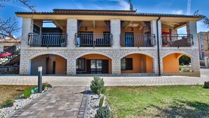 Un bâtiment à deux étages doté d’un balcon à l’étage supérieur, d’une façade en briques et d’une zone d’entrée pavée.
