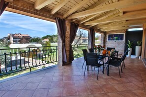 A covered patio with a brick wall, a dining table with chairs, and a view of the surrounding area. - Apartment Tina with Hot Tub (Porec)