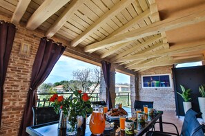 An outdoor patio with a brick wall, wooden ceiling beams, and a table set with breakfast items. - Apartment Tina with Hot Tub (Porec)