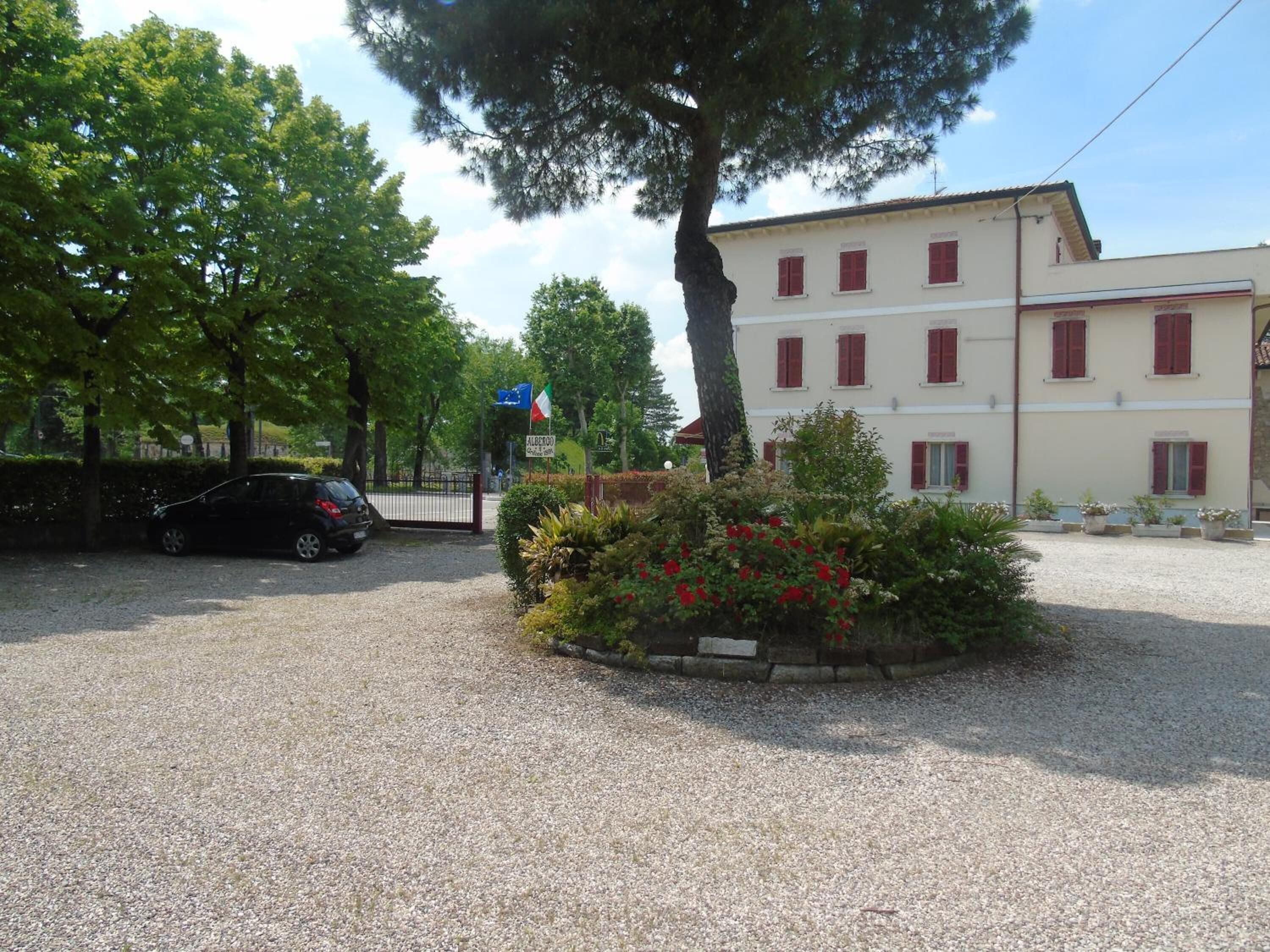 Un edificio con vialetto sterrato, un'auto parcheggiata e una bandiera.