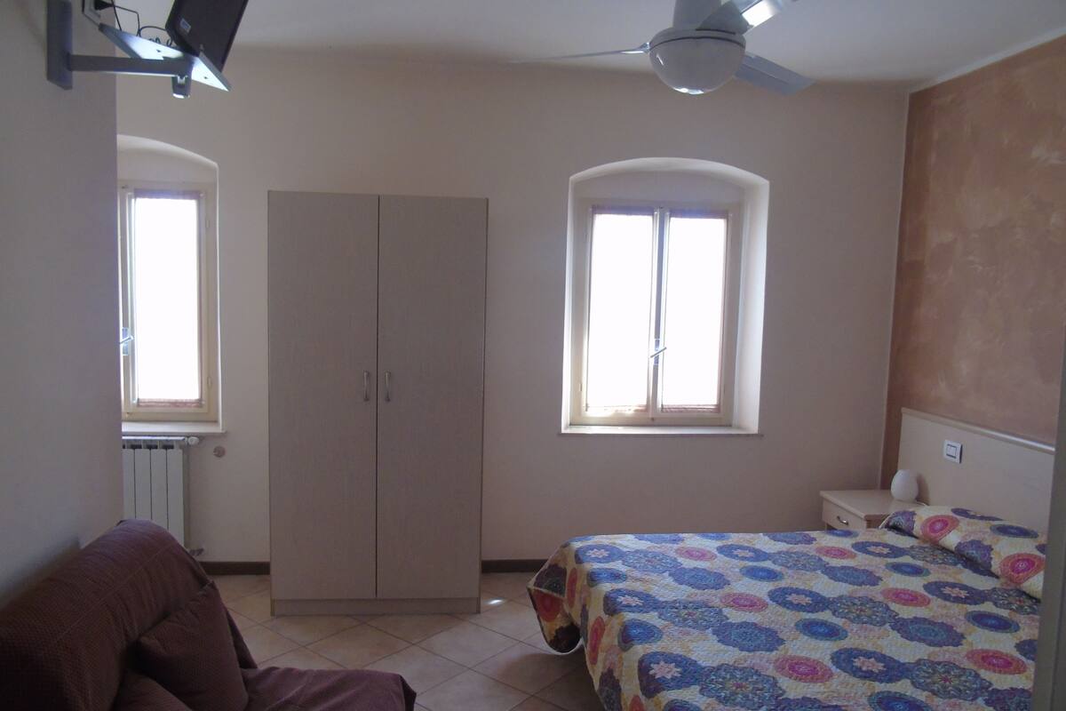 Ein Schlafzimmer mit Bett, Kleiderschrank, Heizkörper, Deckenventilator und Fenster.