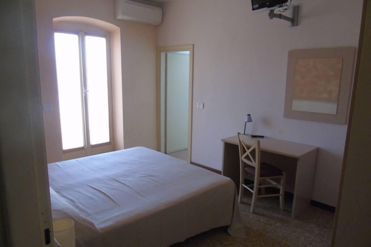 Ein Schlafzimmer mit Bett, Schreibtisch, Stuhl, Fernseher und Fenster.