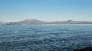 Paesaggio costiero con acque calme, costa rocciosa e montagne in lontananza.