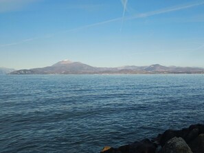 Vista costera con agua tranquila, costa rocosa y montañas a lo lejos.