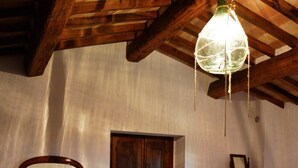 Een kamer met een rustiek houten plafond, een radiator, twee fauteuils, een bed met een rode deken, een houten kast en een spiegel aan de muur.