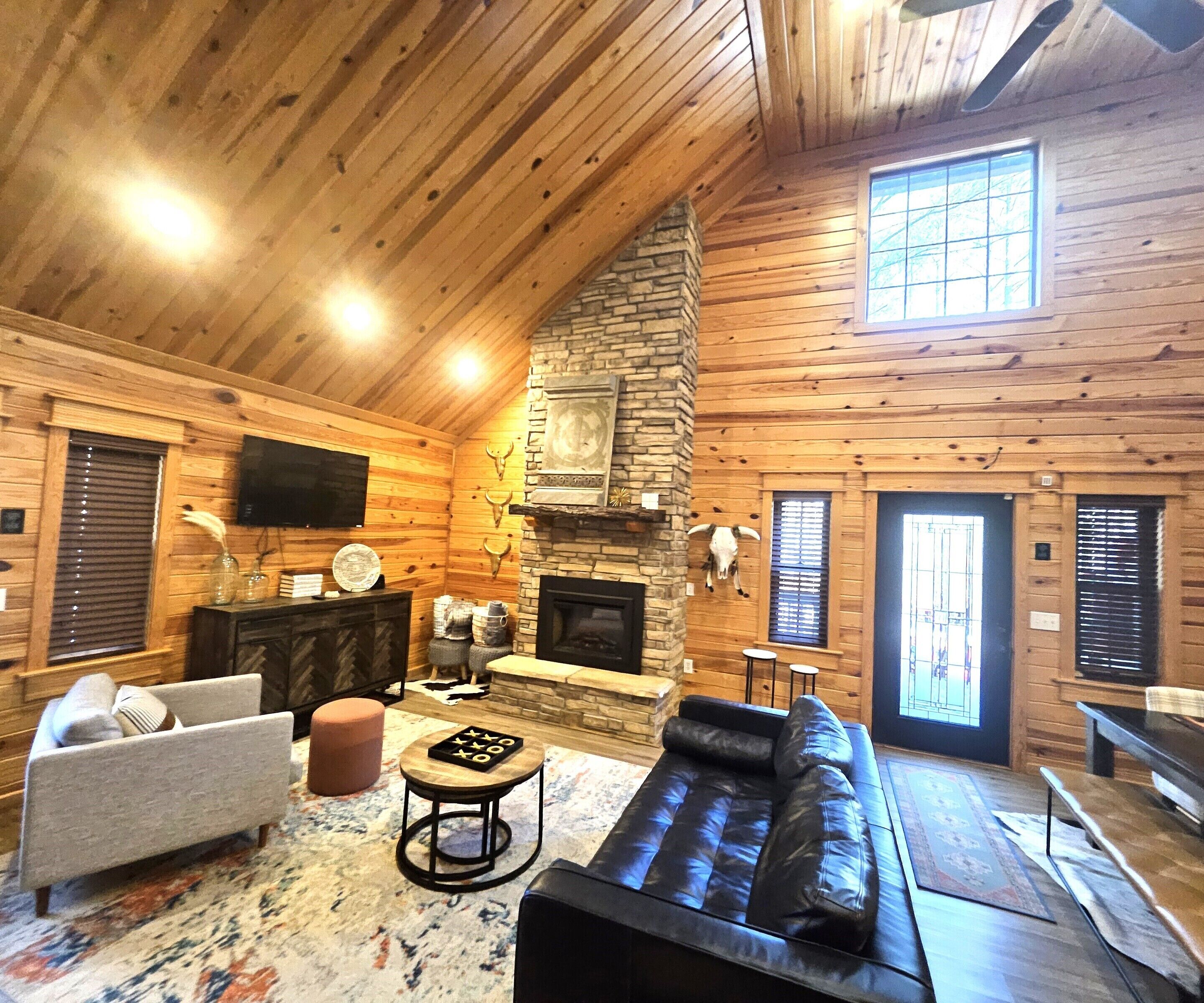 A log cabin interior with a stone fireplace, a leather sofa, a television, and a rustic decor.