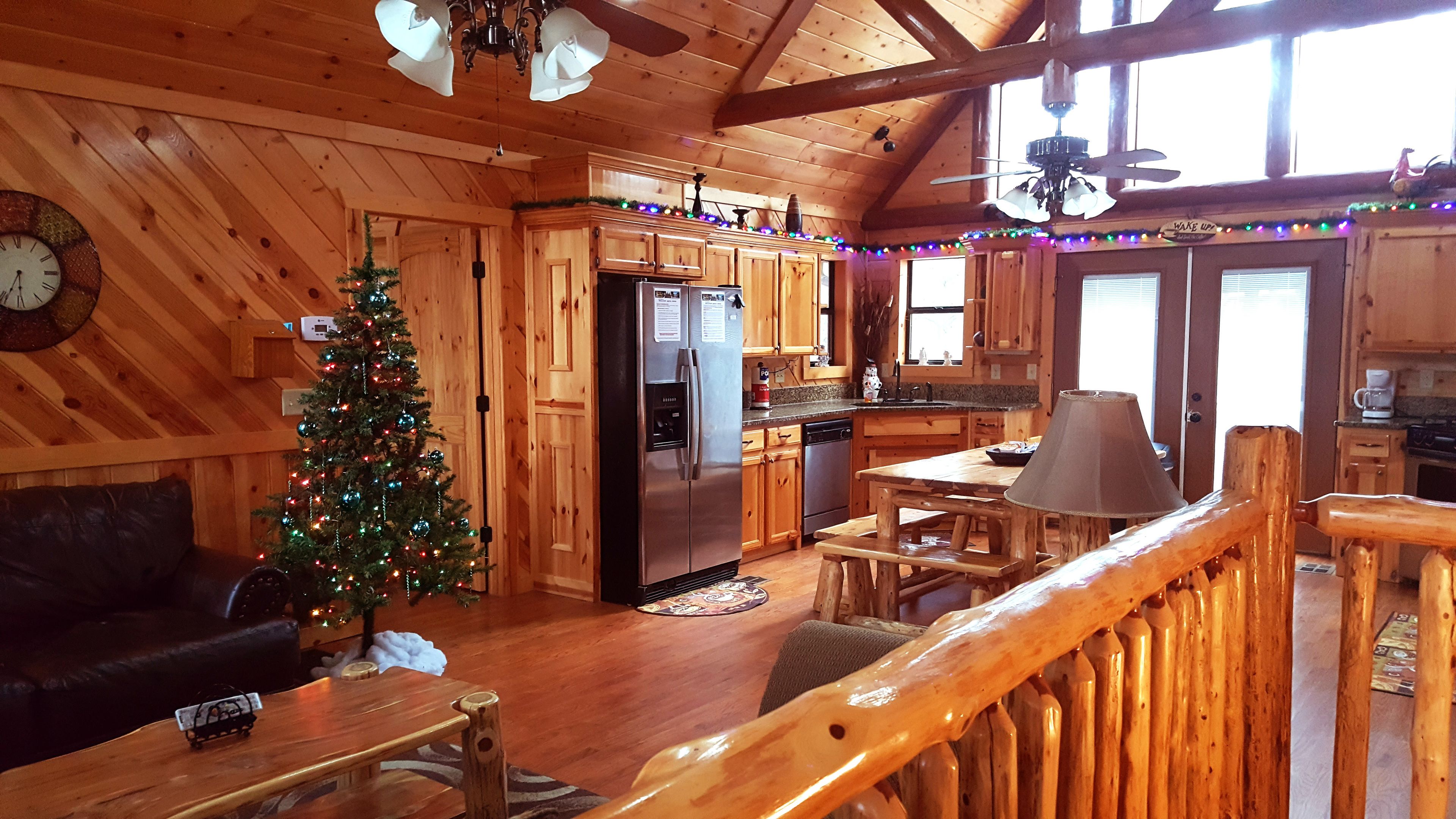 A wooden cabin interior with a kitchen, dining area, and a Christmas tree.