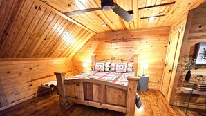 Ein Zimmer mit Holzwänden, einem Bett, einem Deckenventilator und einem kleinen Tisch mit einer Lampe.