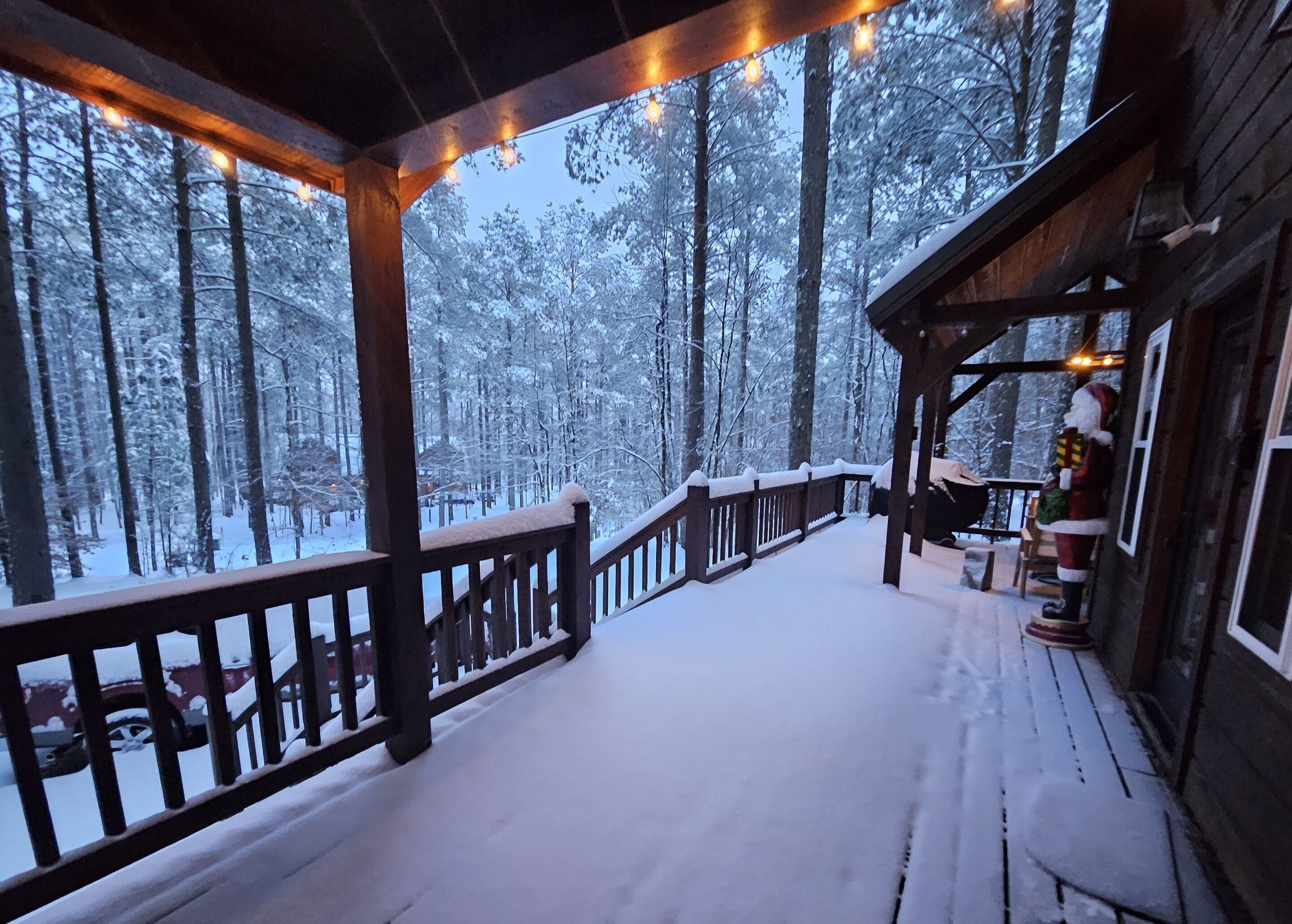 A wooden deck with a railing, surrounded by snow-covered trees.