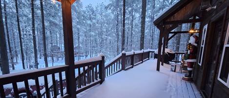 A wooden deck with a railing, surrounded by snow-covered trees.