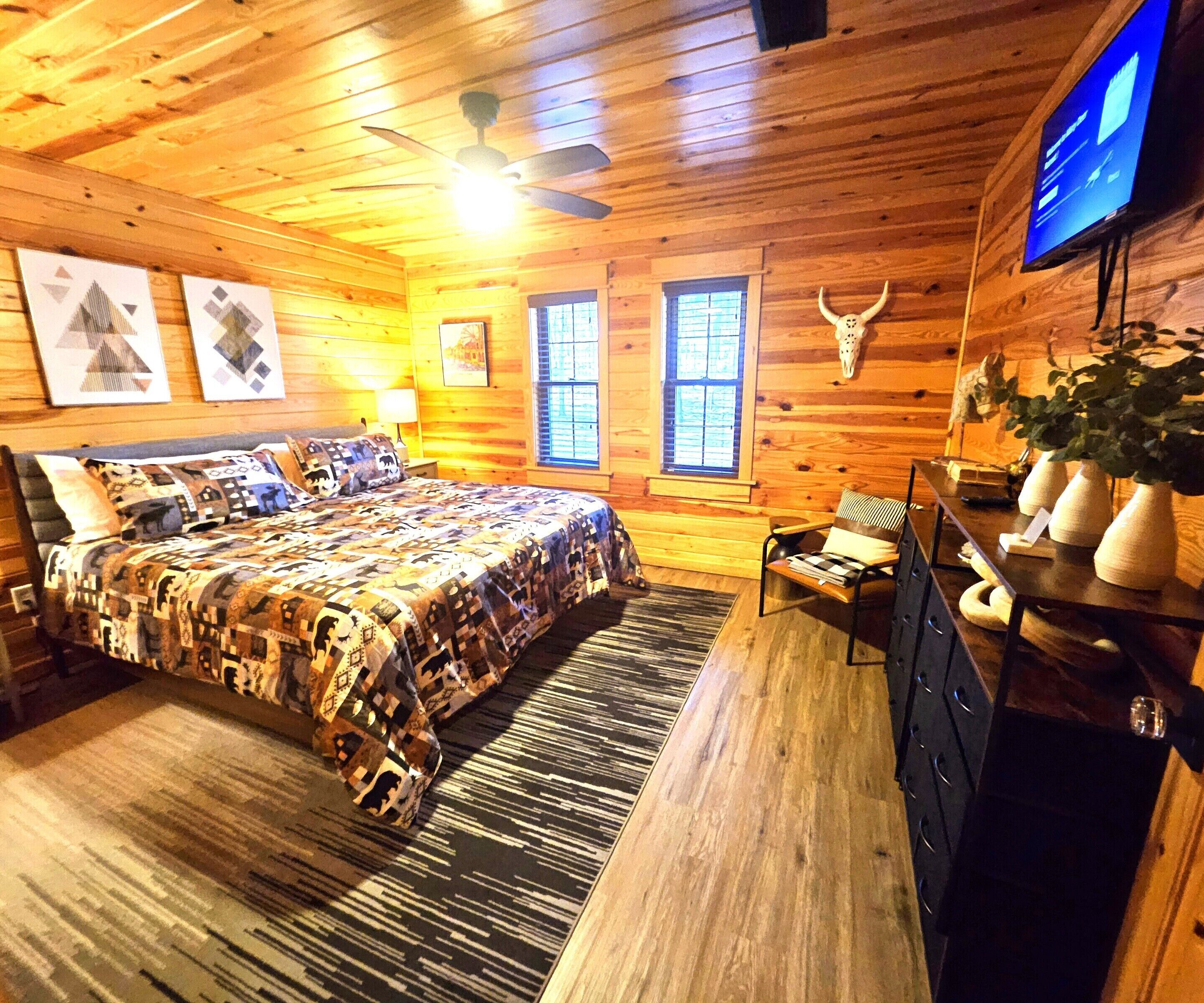 Une chambre aménagée dans un chalet en rondins, avec un lit, un bureau, une télévision et une fenêtre.