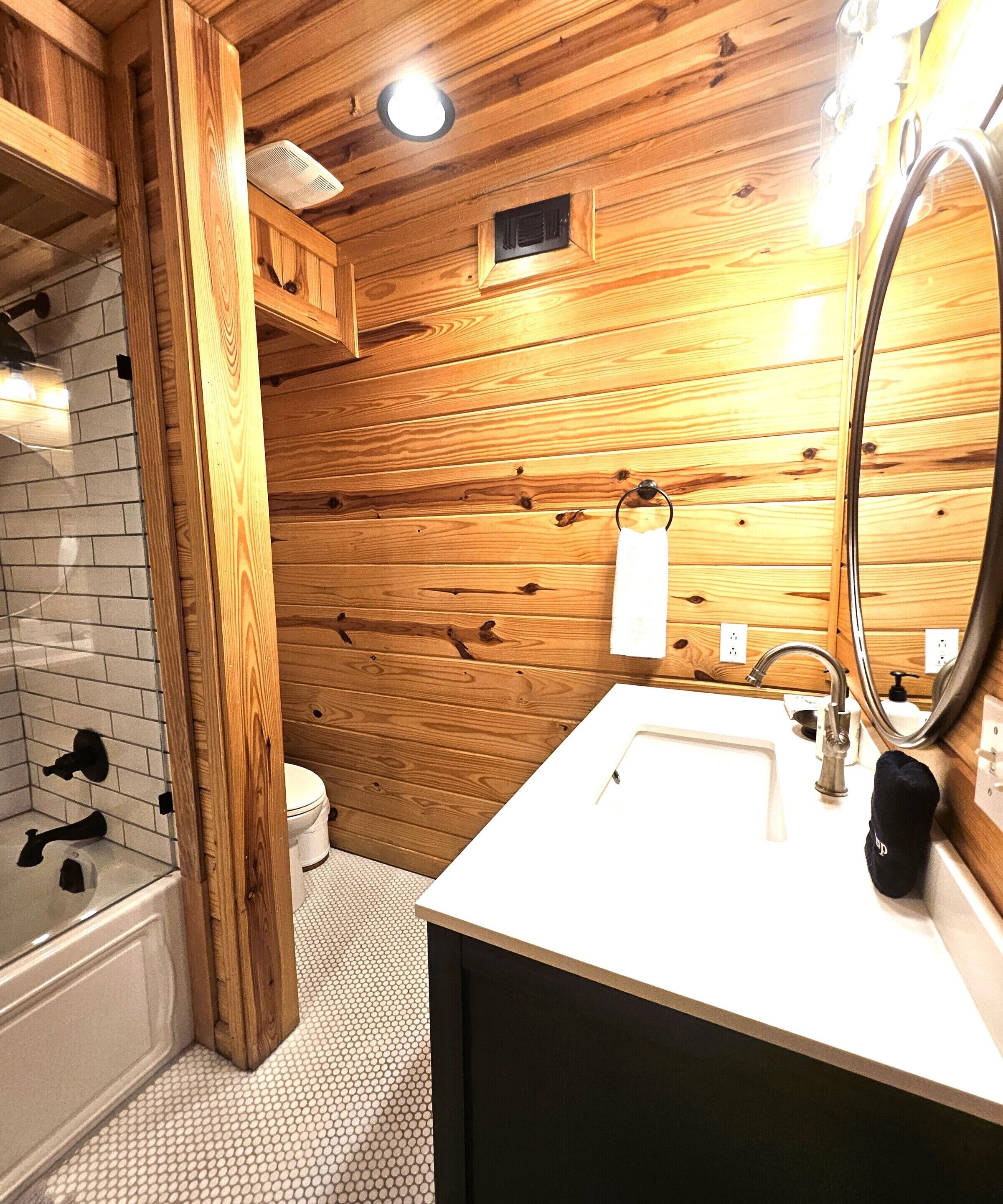 A wooden-paneled bathroom with a white sink, a mirror, and a toilet.