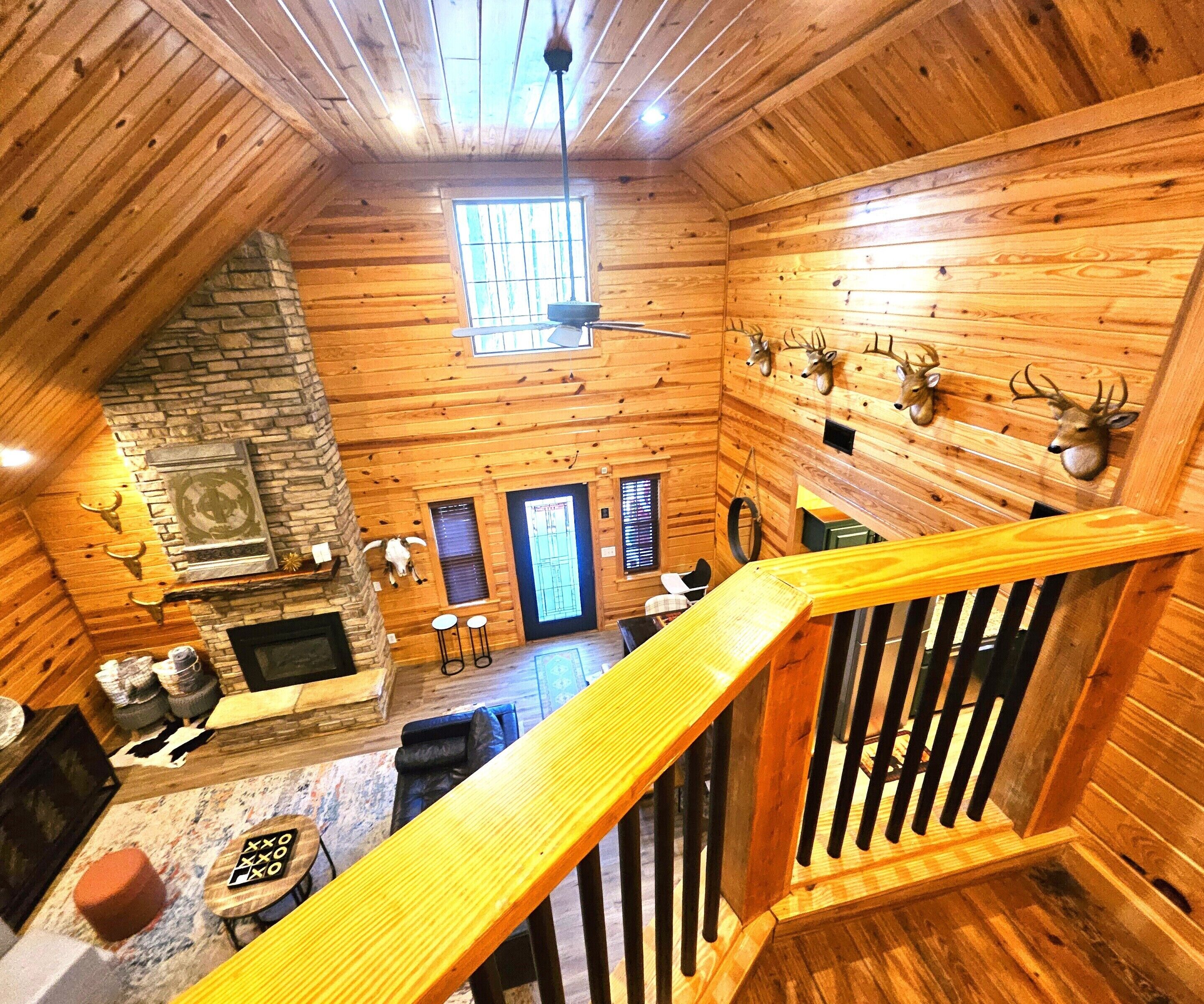 A log cabin interior with a stone fireplace, wooden walls, and mounted animal heads.