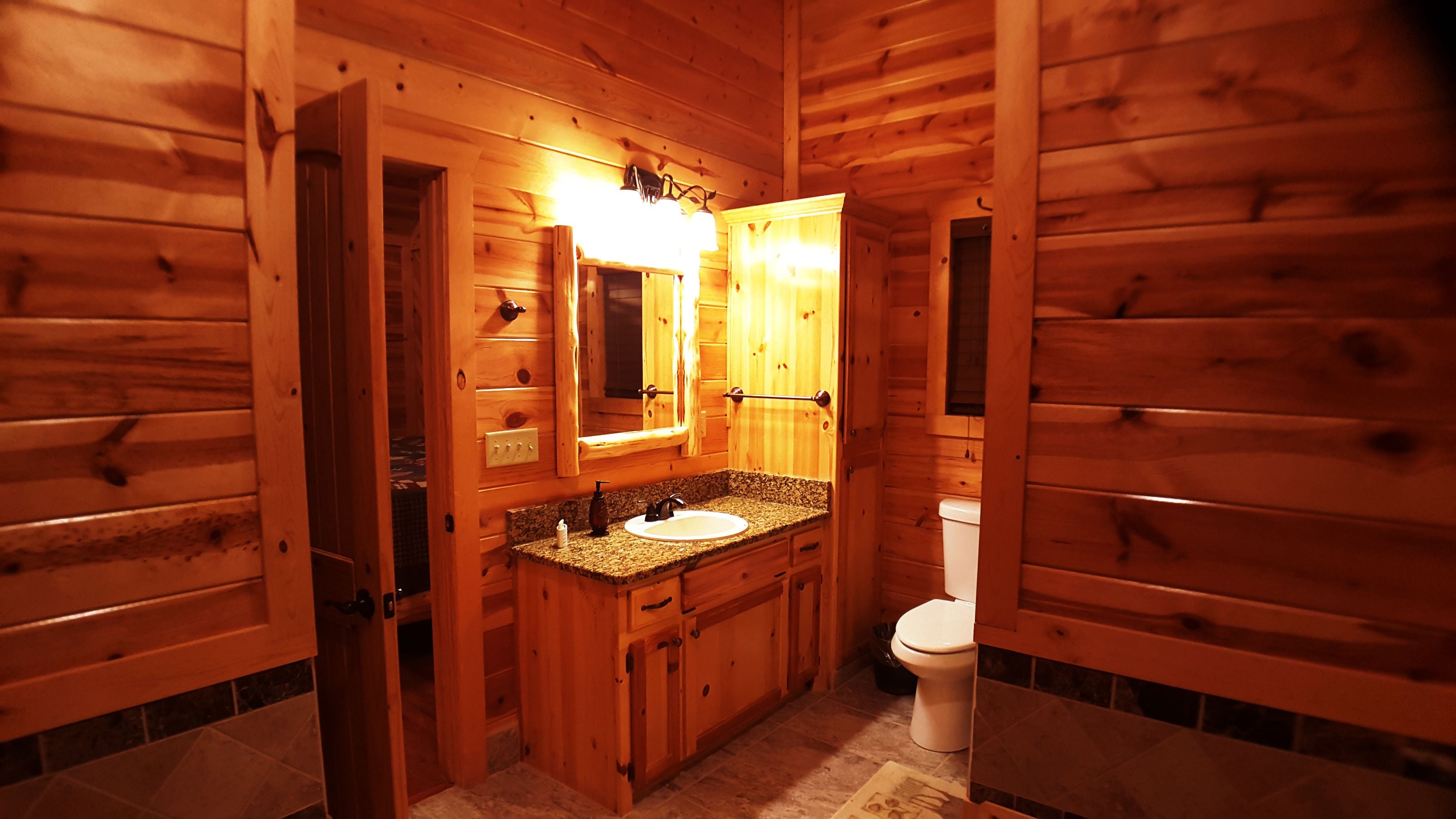 Een houten badkamer met een granieten wastafelblad, een wastafel, een spiegel en een toilet.