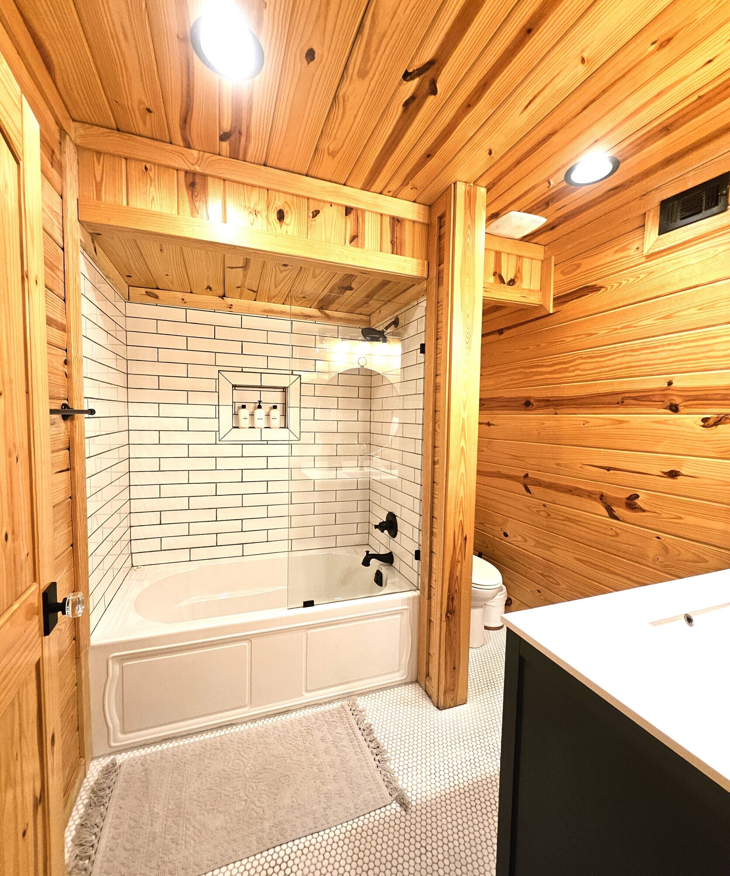 A wooden cabin bathroom with a white-tiled shower wall, a freestanding bathtub, and a wooden vanity.