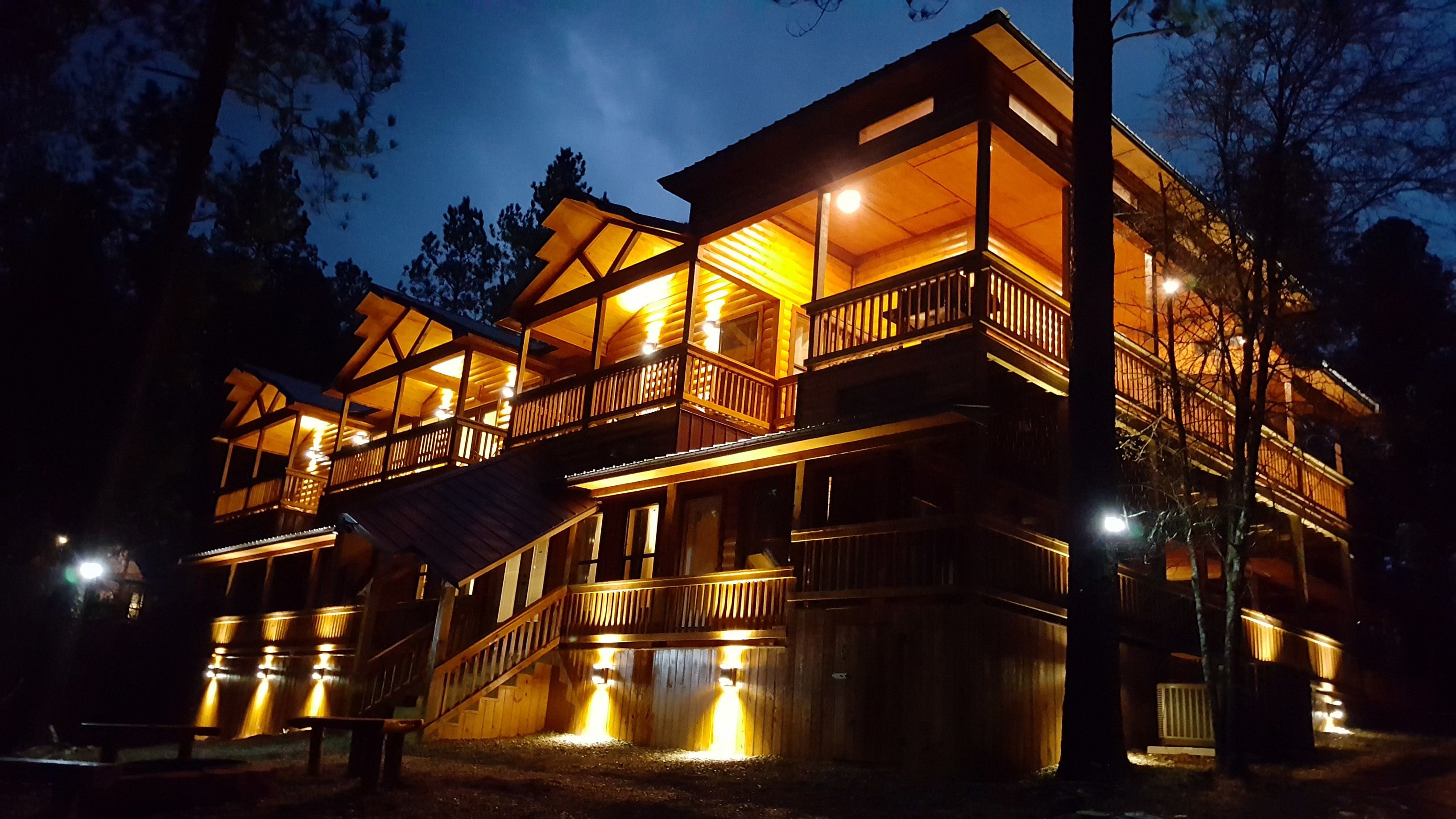 A multi-story wooden cabin with balconies and a staircase, illuminated at night.
