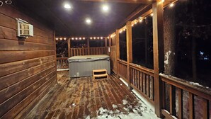 Eine Holzterrasse mit Whirlpool, Lichterketten und Blick auf die Umgebung.