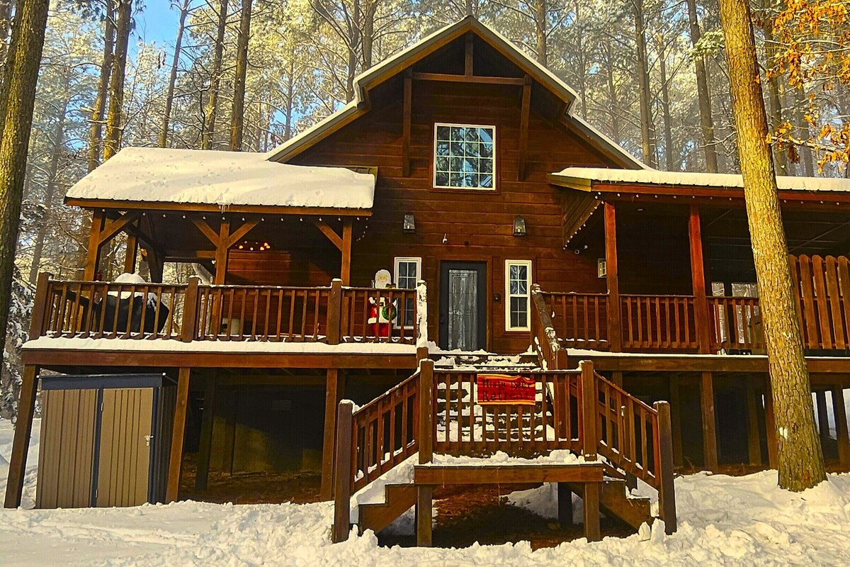 Eine Holzhütte mit Balkon und überdachter Veranda, umgeben von schneebedeckten Bäumen.