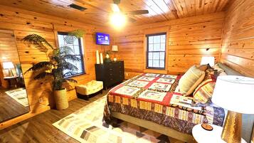 A cozy cabin-style room with a wooden interior, a bed with a patterned quilt, a television, and a window with blinds.