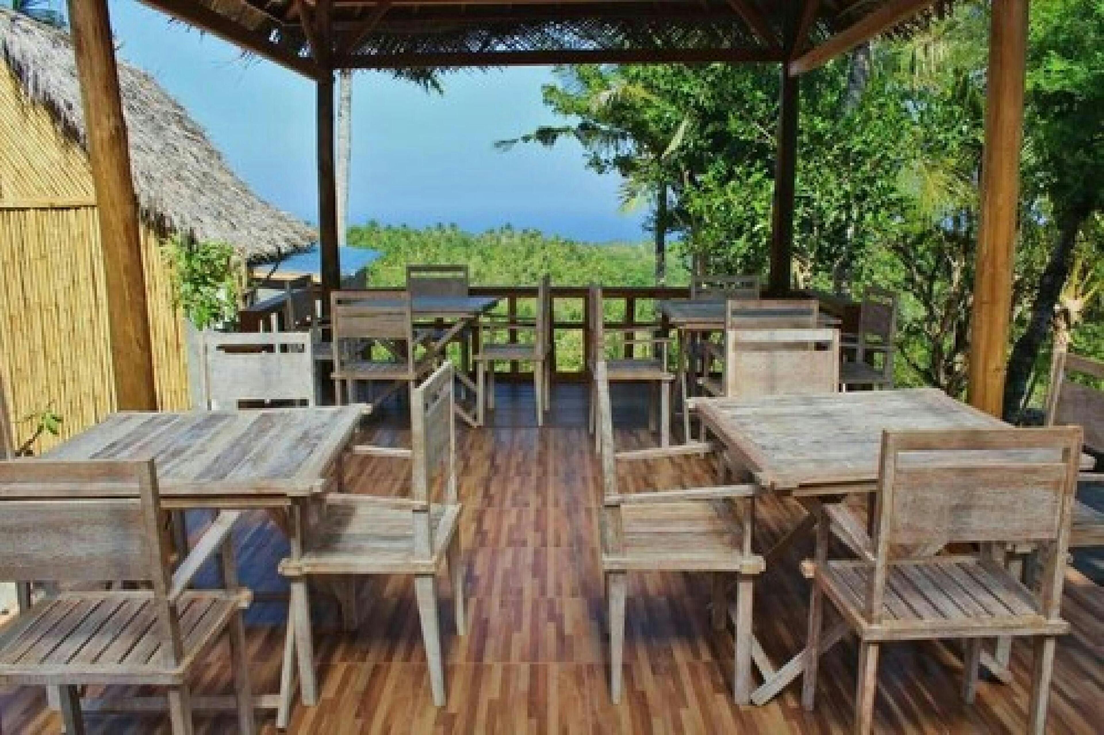 An outdoor wooden deck with tables and chairs, surrounded by a bamboo fence and tropical vegetation.
