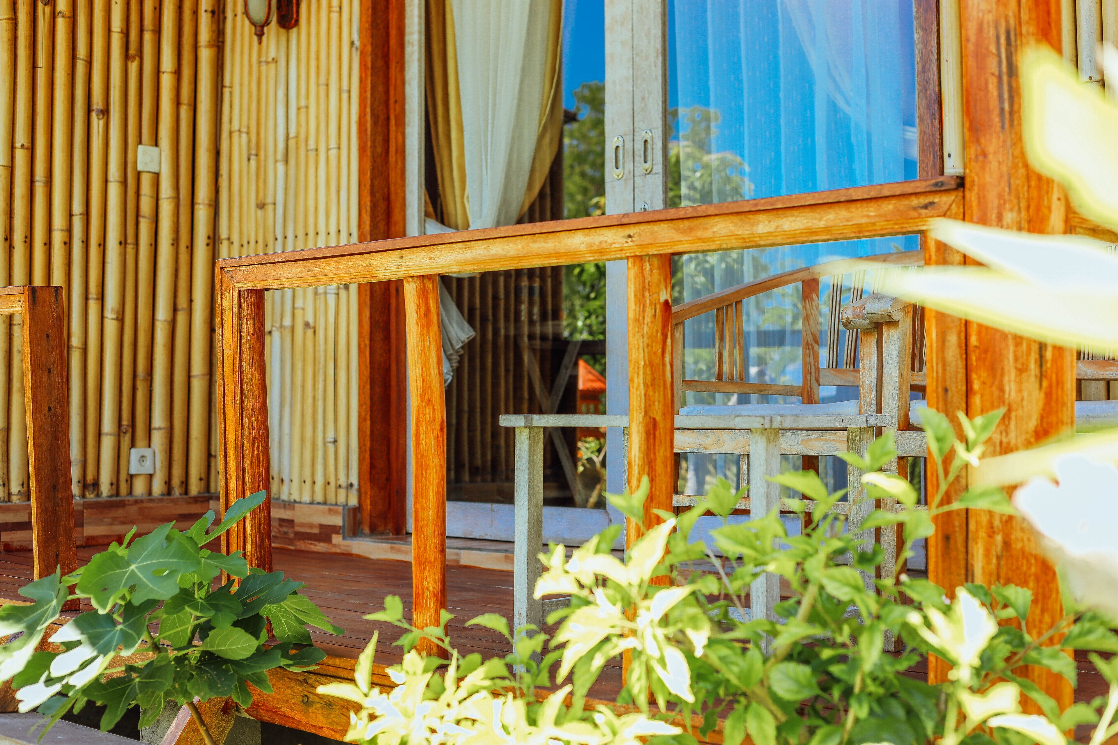 A wooden deck with a glass door leading to a room, surrounded by bamboo walls and plants.