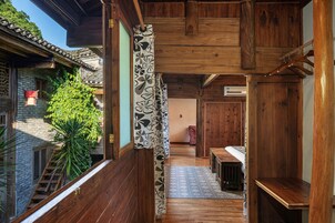 Un interior de madera tradicional con una escalera que lleva a un balcón, una cortina con estampado y vistas a un árbol exterior.
