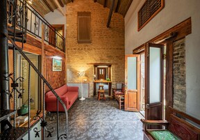 Un interior rústico con una escalera de madera, un sofá rojo, un banco de madera y un suelo estampado.