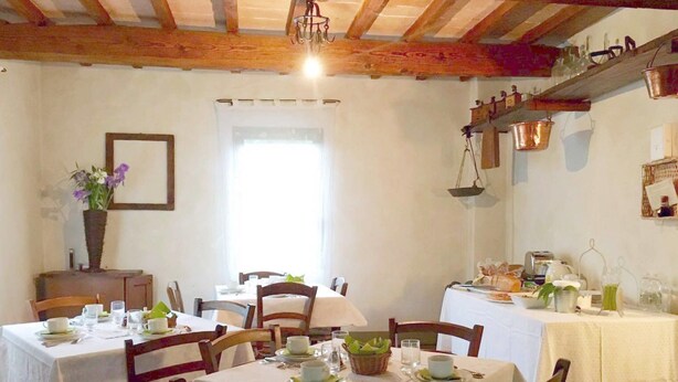 Un espace repas avec des tables et des chaises en bois, des nappes blanches et un plafond rustique aux poutres apparentes.