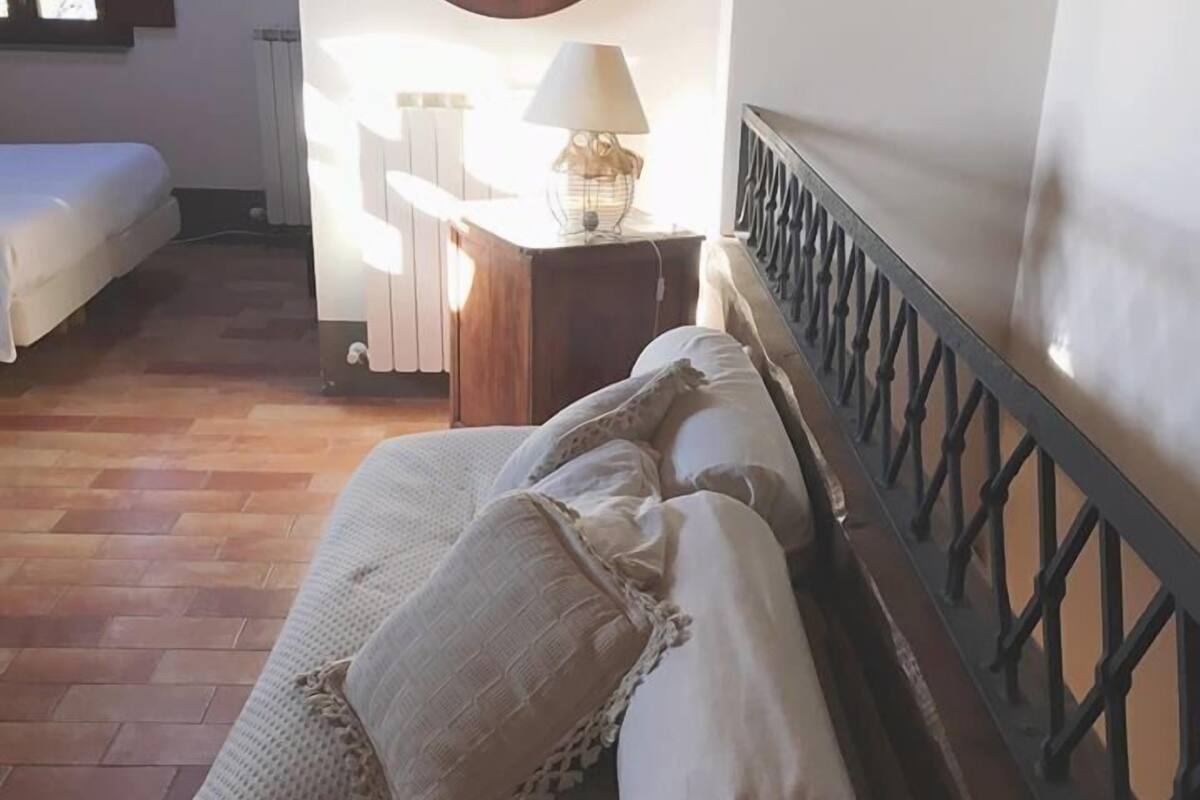 Un dormitorio con cabecera de madera, una cama con ropa de cama blanca, un adorno circular en la pared y una mesita de noche con lámpara.