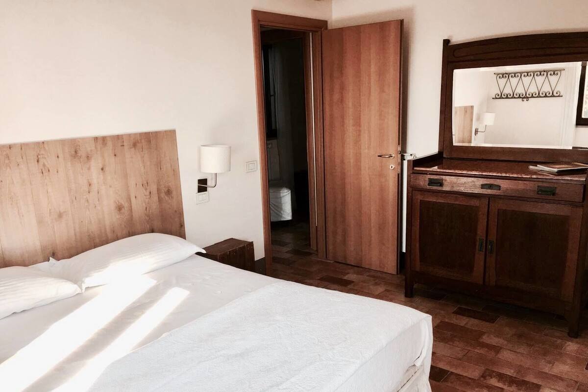 Habitación de hotel con cabecera de madera, cama con ropa blanca, armario de madera y un espejo sobre el armario.