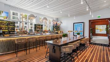 Un bar moderno con una barra larga, varios taburetes y una variedad de botellas y vasos.
