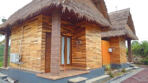 A wooden cabin with a thatched roof, a small porch, and a stone foundation. - Batang Golden Hills Villa (Penida Island)