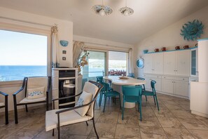 Een eetgedeelte met uitzicht op zee, een keuken met witte kasten en een eettafel met stoelen.