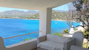 Un balcon doté de meubles en osier, d’un sol carrelé et offrant une vue sur la mer et les montagnes.