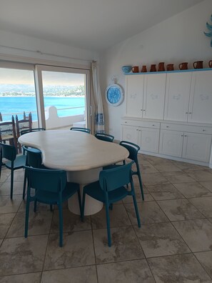 Ein Essbereich mit einem runden Tisch, Stühlen, Meerblick und weißen Schränken mit dekorativen Griffen.
