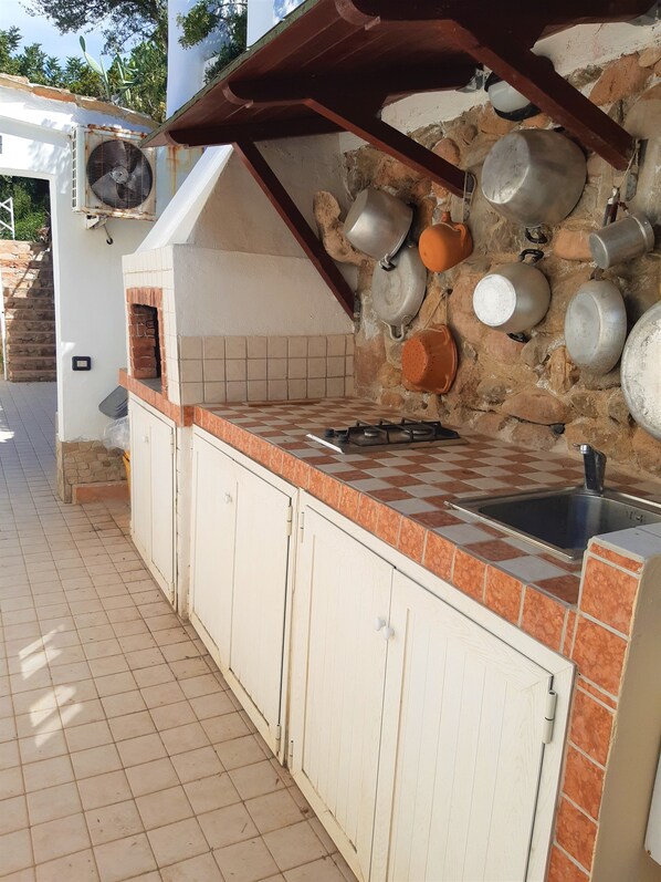 Een keuken met een zwart-wit betegelde spatwand, een gasfornuis en hangende pannen.