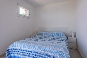 Een slaapkamer met een bed, twee nachtkastjes, een raam en een wandlamp.