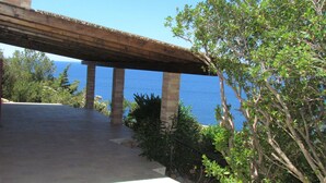 Un espace extérieur abrité, avec vue sur la mer, soutenu par des piliers en briques et entouré de verdure.
