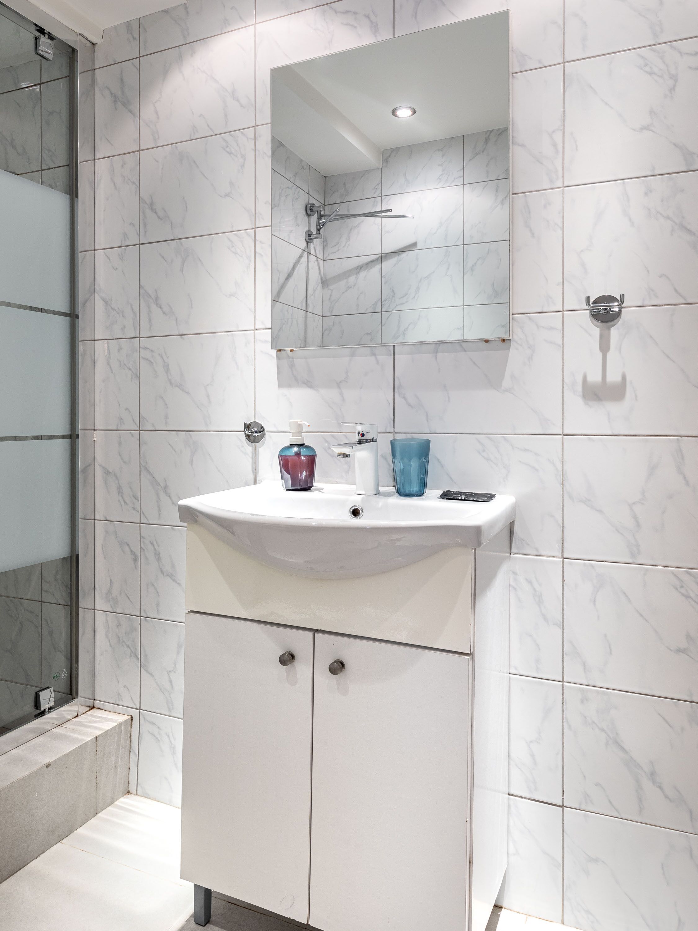 Een badkamer met een wit marmeren wastafel, een spiegel en een douche.