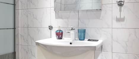 A bathroom with a white marble sink, a mirror, and a shower.