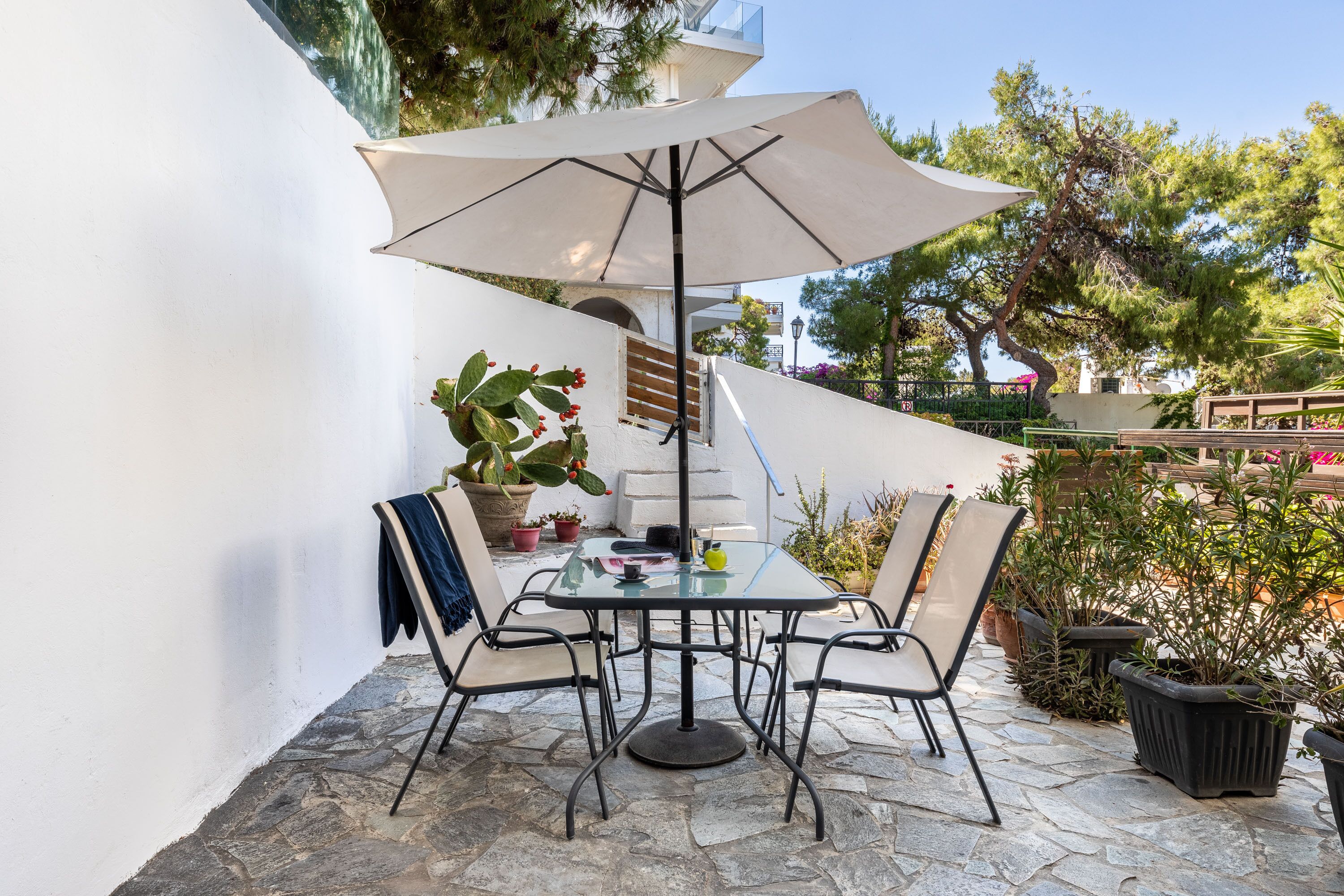 Une terrasse extérieure avec une table ronde, quatre chaises, un grand parasol et des plantes en pot.