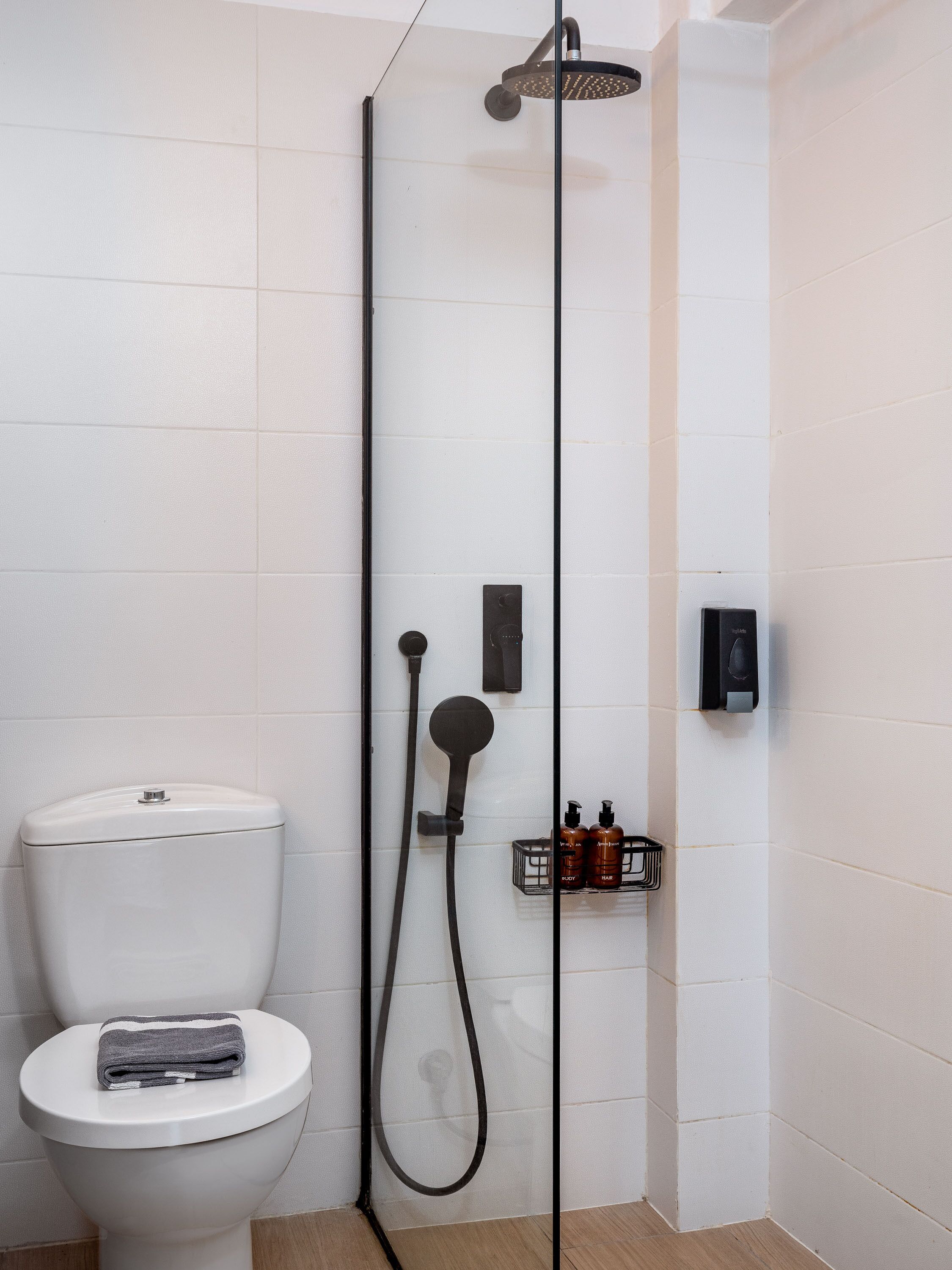 Une salle de bain moderne avec des toilettes blanches, un espace douche et une petite étagère contenant des articles de toilette.