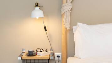 Een slaapkamer met een houten bed, een nachtkastje met een lamp, een kopje en glazen, en een stopcontact aan de muur.