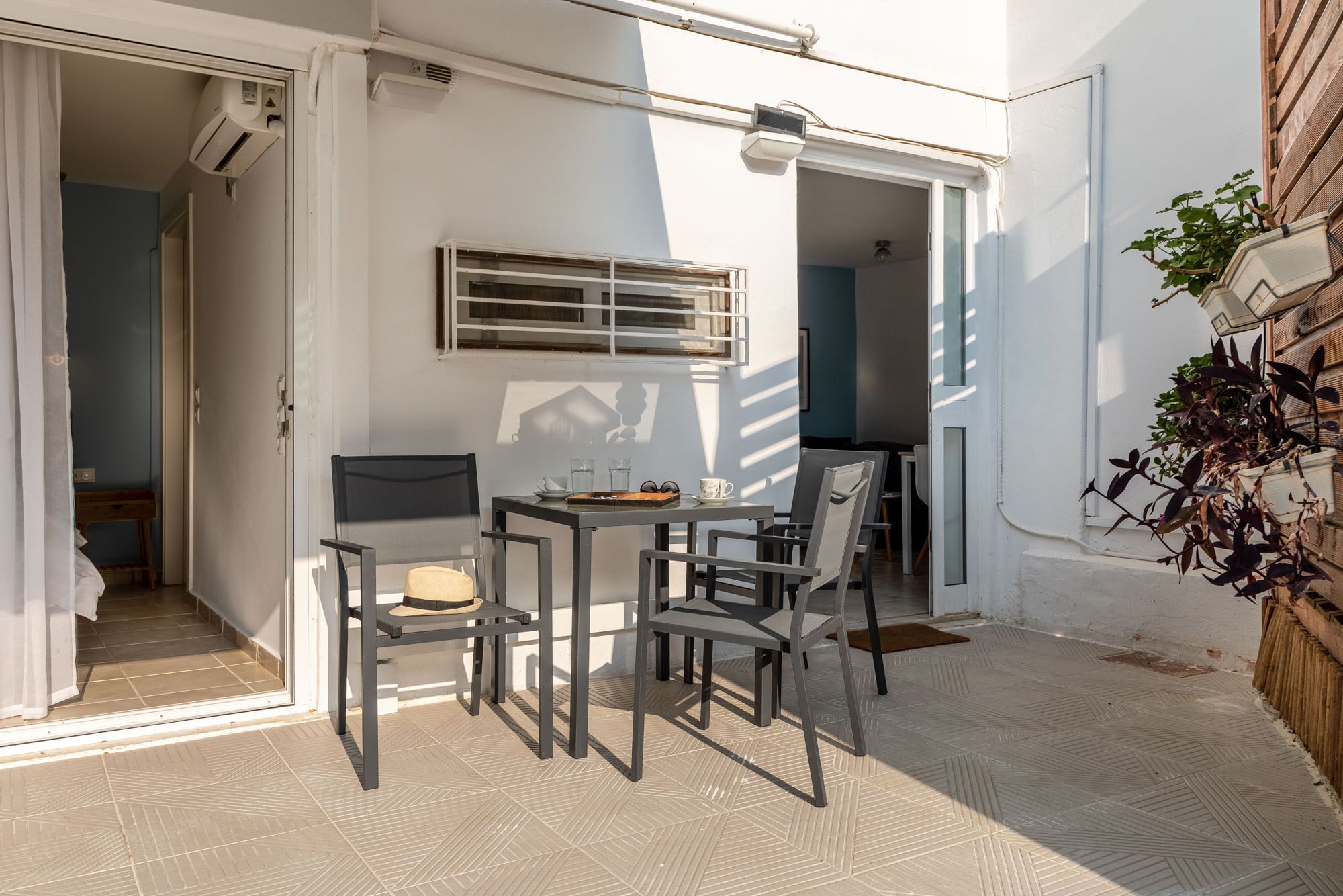 Eine kleine Terrasse im Freien mit Tisch und Stühlen, ein Fenster mit Metallgitter und ein Blumentopf.