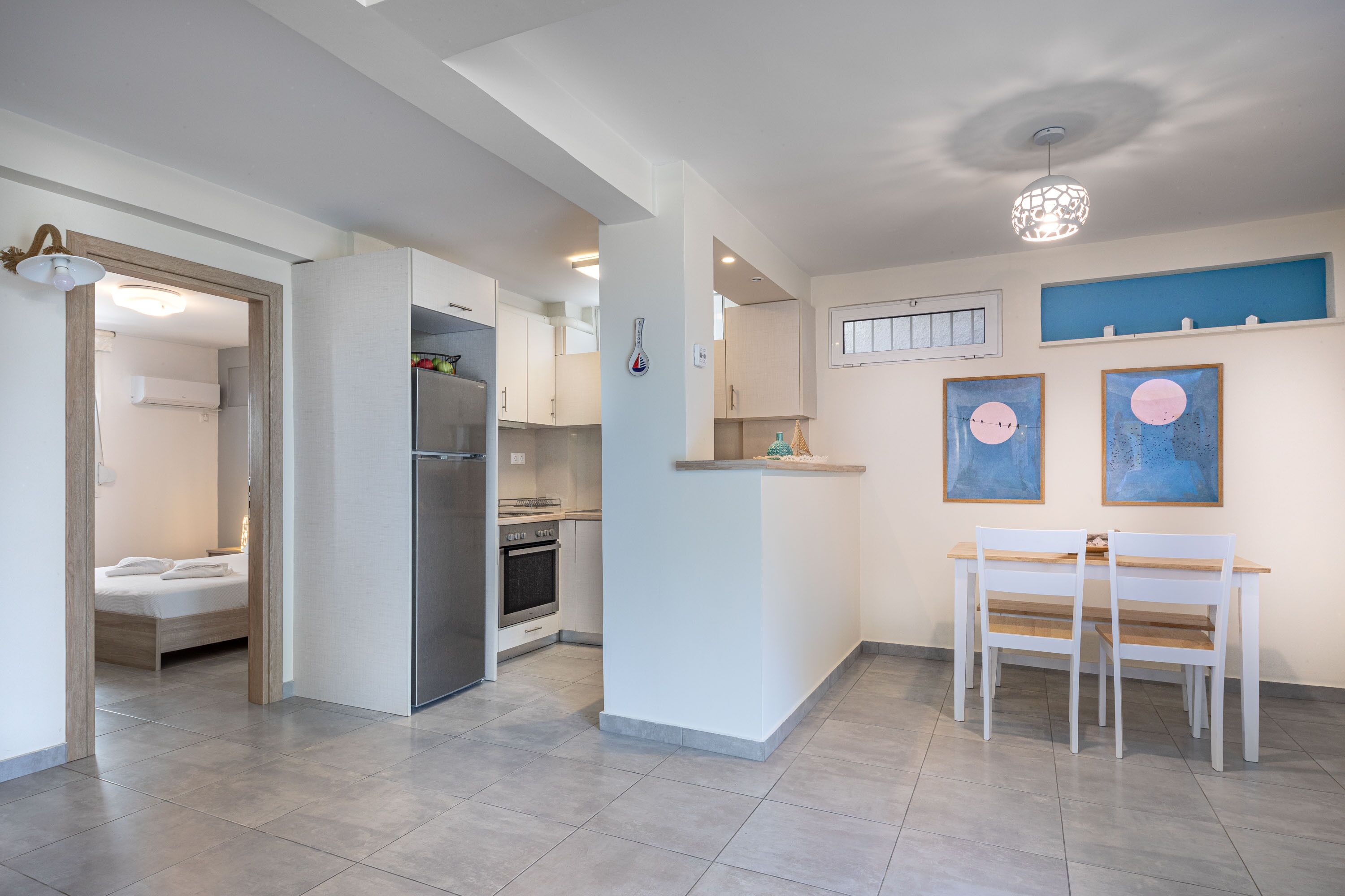 A modern kitchen with white cabinets, a refrigerator, and a dining area with a white table and chairs.