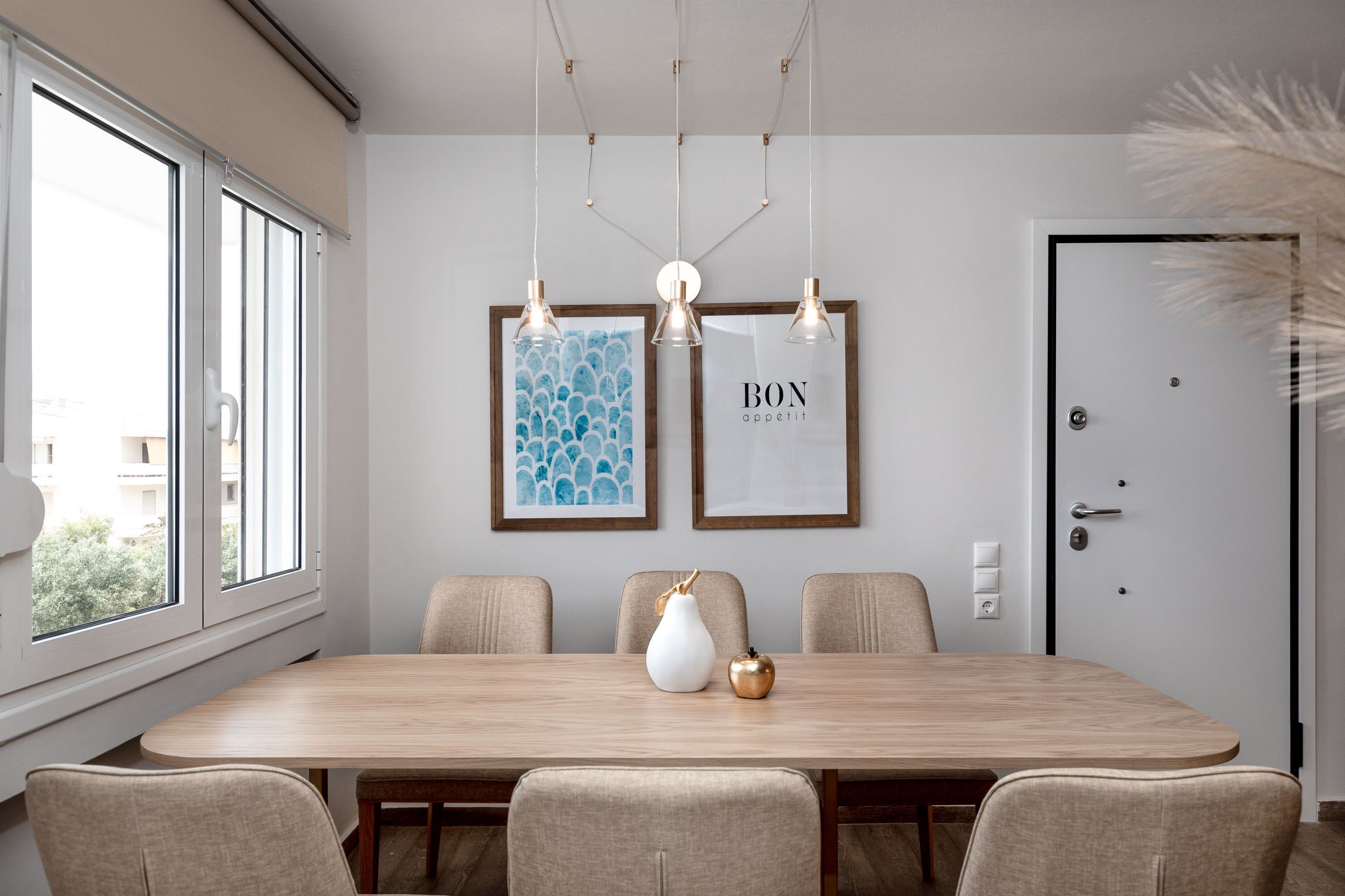 A dining area with a wooden table, six chairs, and two framed artworks on the wall.