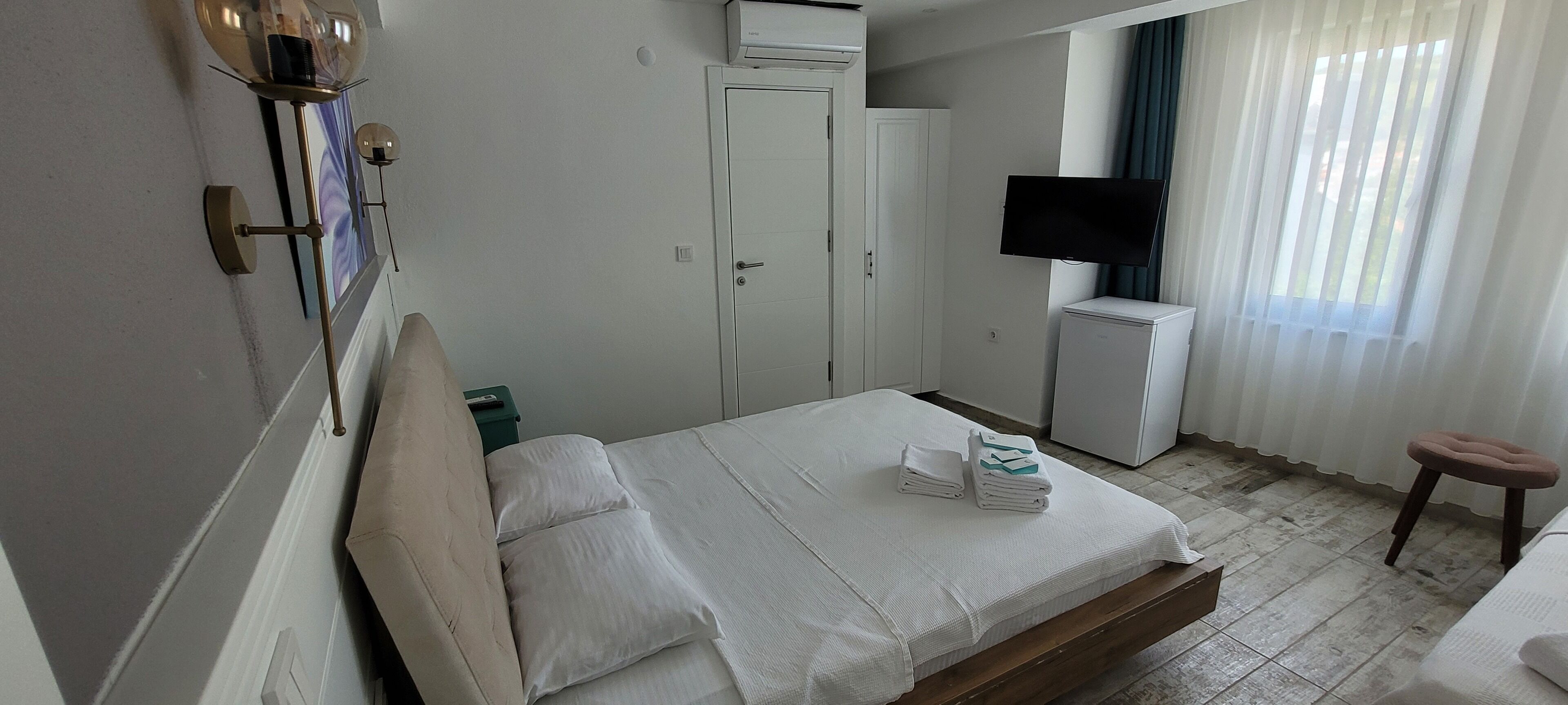 A hotel room with a bed, a TV, a wardrobe, a desk, and a chair.