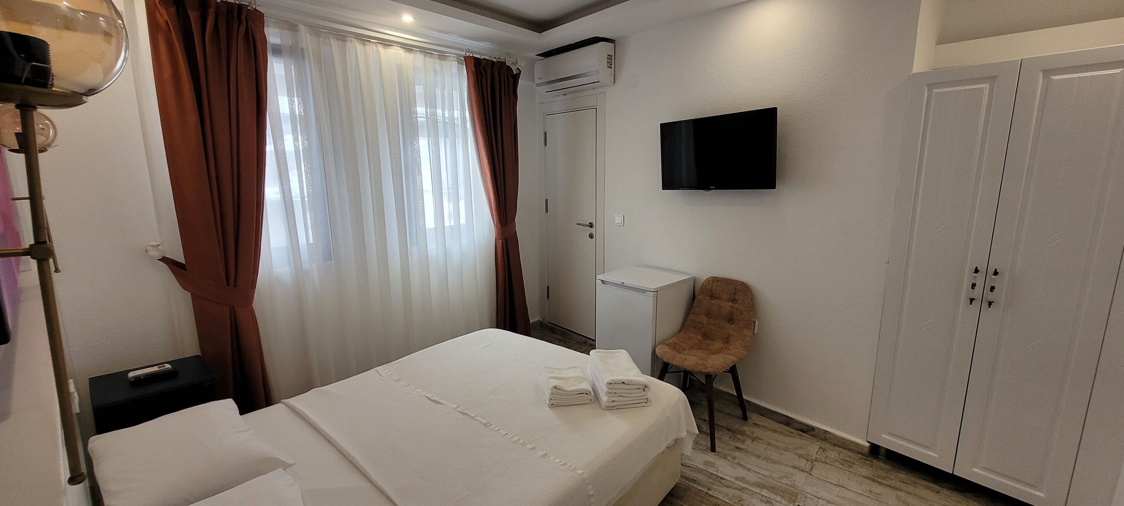 A hotel room with a bed, a chair, a TV, and a wardrobe.