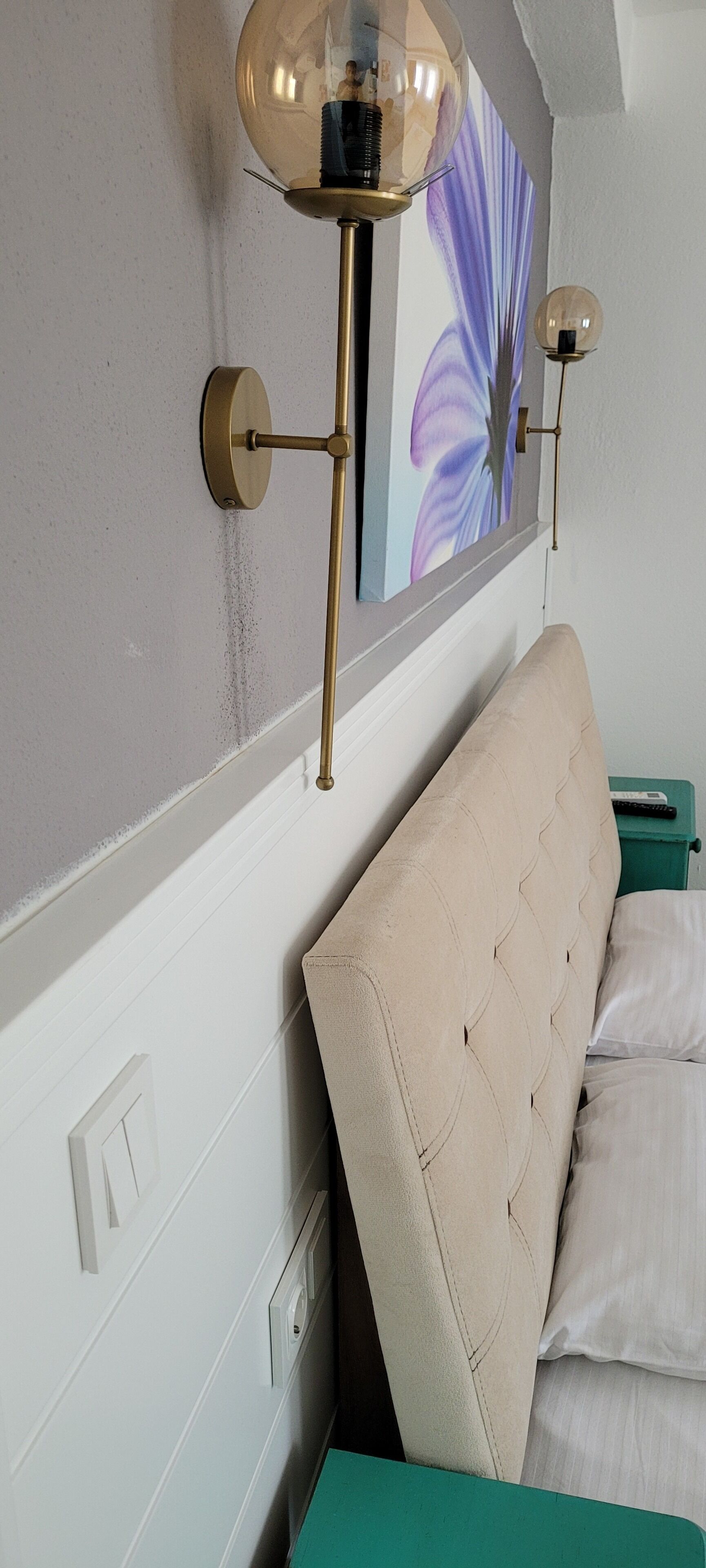 A bedroom with a tufted headboard, a green nightstand, and two wall-mounted lamps.