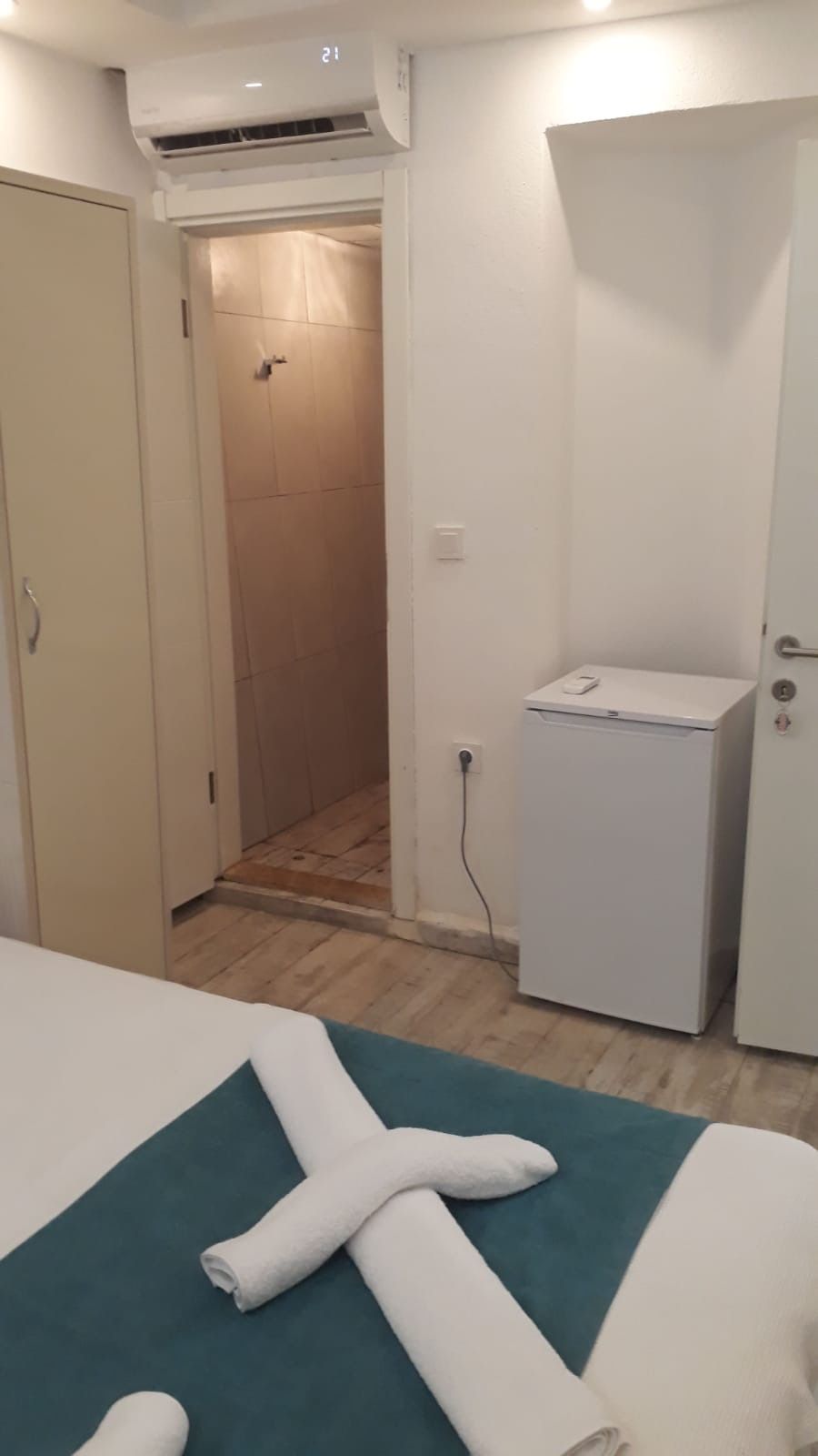 Une chambre d’hôtel avec un lit, une petite armoire blanche et une porte donnant accès à une salle de bain.